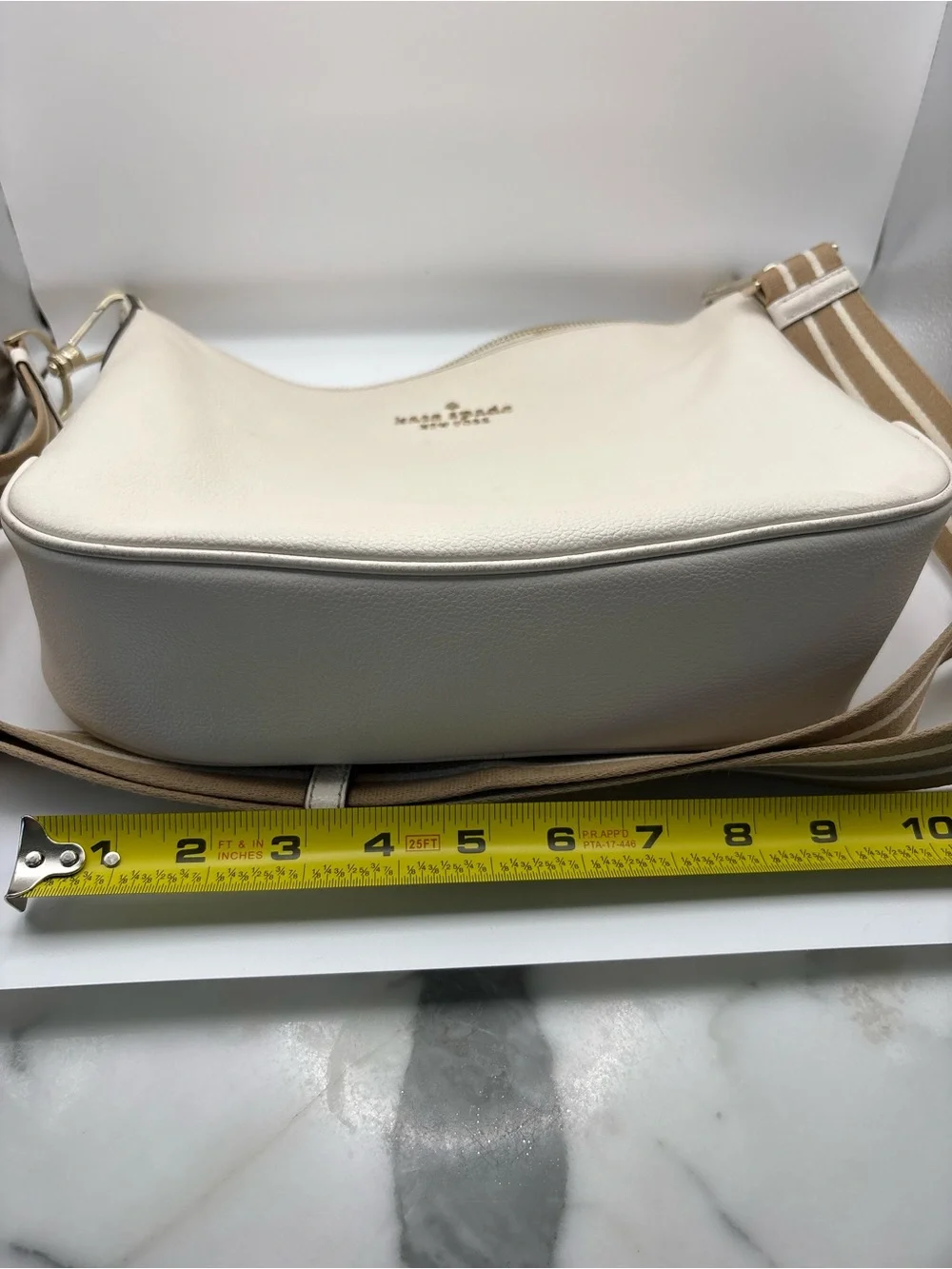 Kate Spade New York cream leather crossbody bag featuring a striped webbing Stra